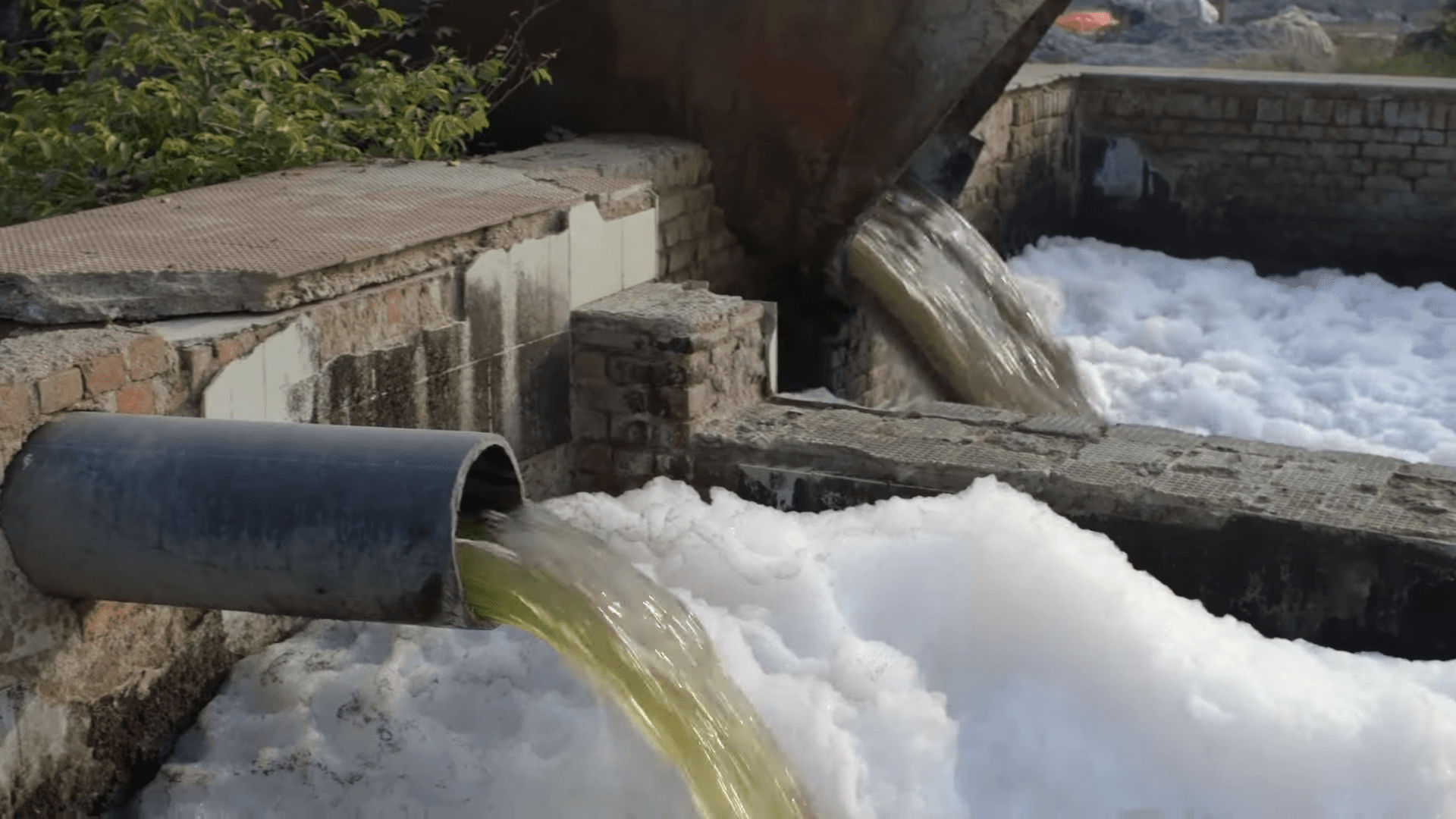 Industrial wastewater flowing from a pipe into a river near factory smokestacks